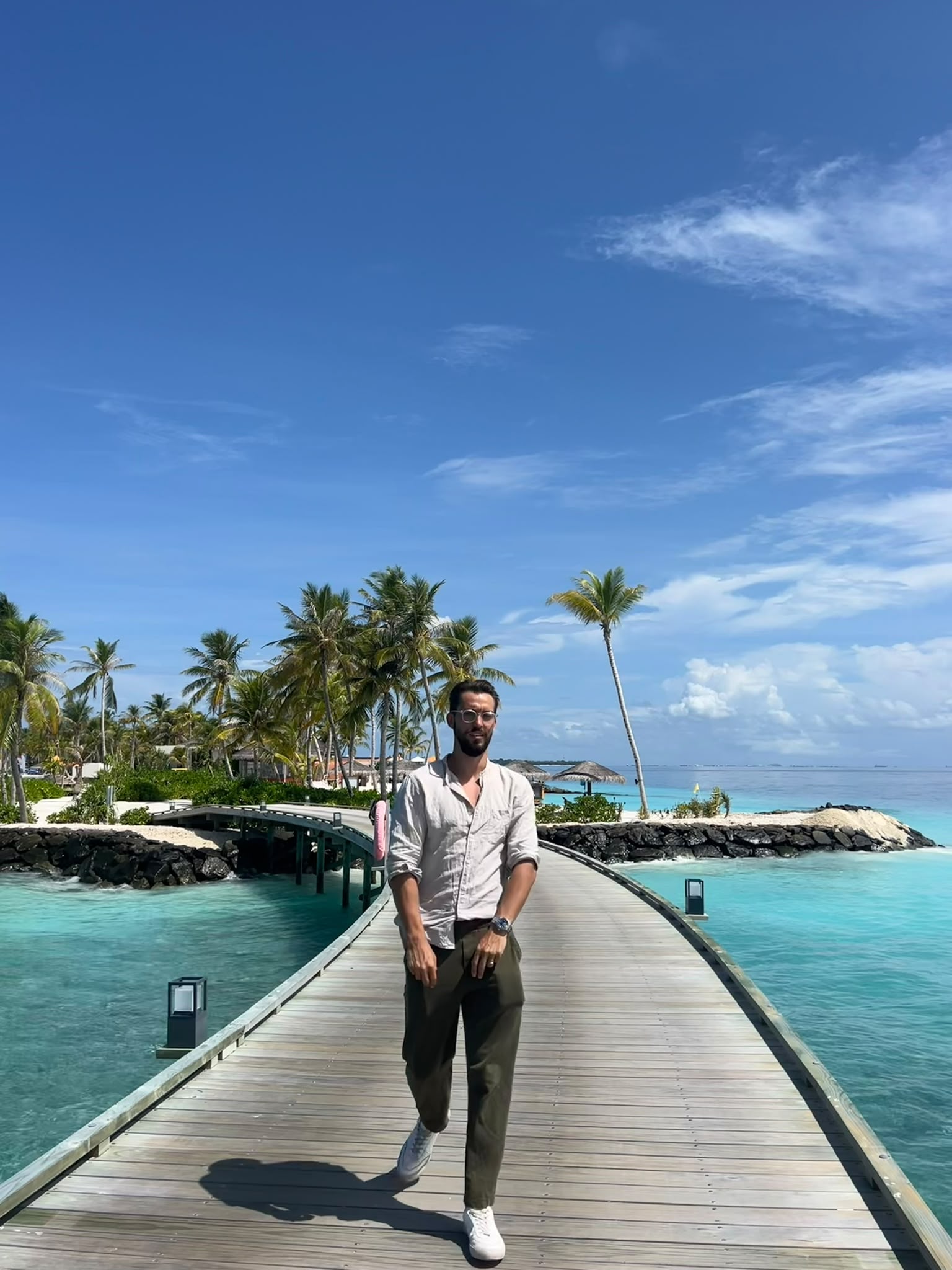 On a wooden boardwalk above turquoise water, with palm trees behind