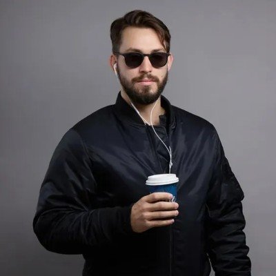 Wearing sunglasses and a black jacket, holding a takeaway coffee