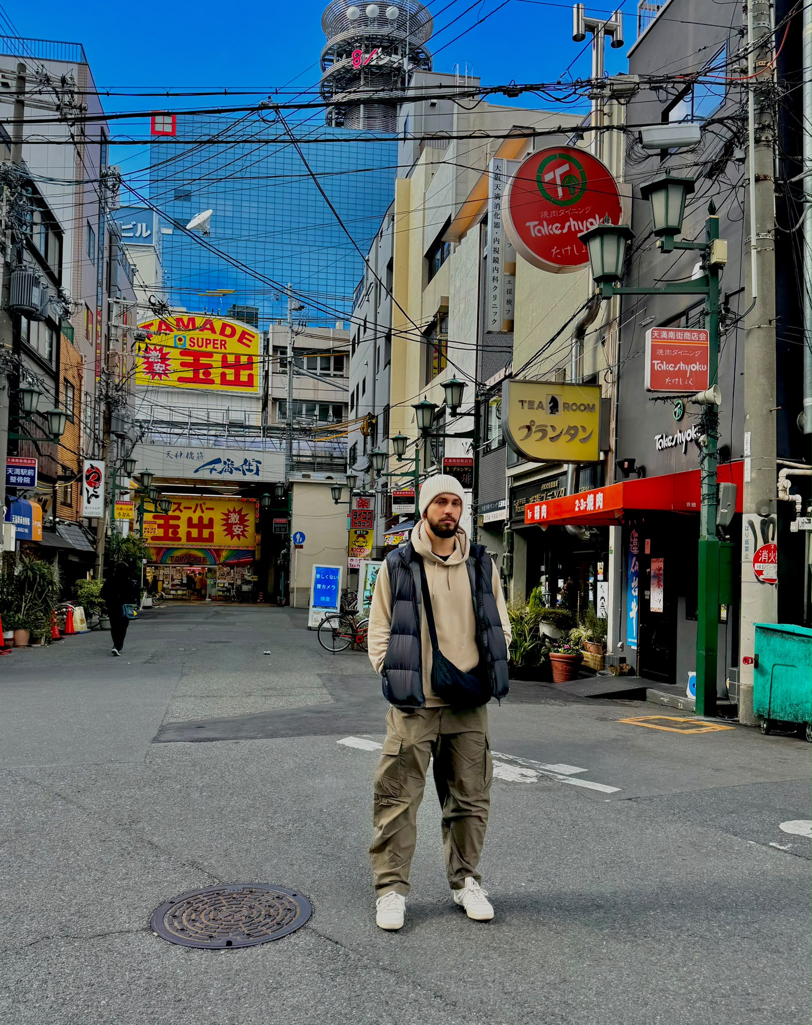 Wearing a beanie and padded vest on a street lined with Japanese shop signs